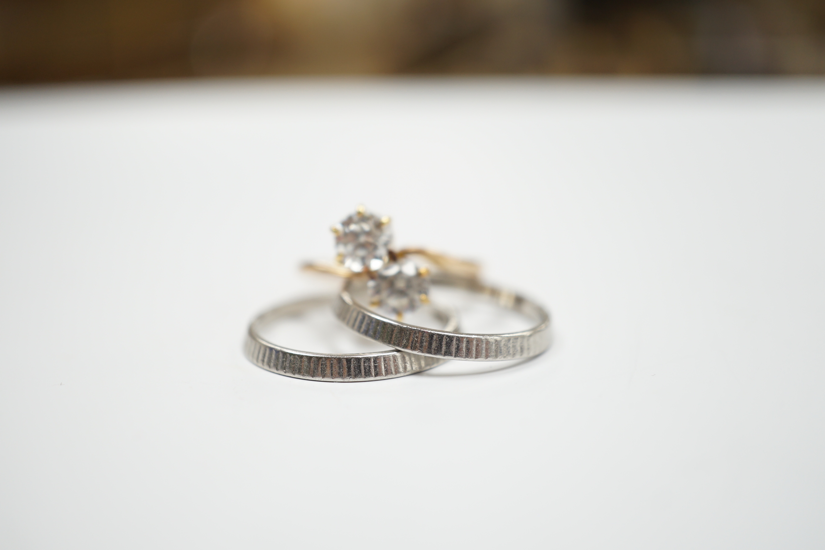 Two white metal bands (stamped platinum) with milled finish, 5.4 grams, together with a 14k and two stone white zircon set crossover ring, gross weight 2.3 grams.